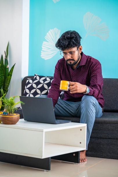 年轻人在笔记本电脑上工作，坐在家里的沙发上喝茶或咖啡。图片下载