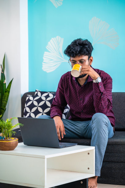 商人拿着咖啡杯在办公室的笔记本电脑上工作。图片下载