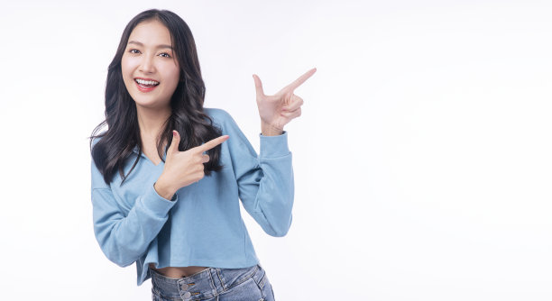 欢快兴奋的亚洲妇女用手指指着一边与产品或空的复制空间站在孤立的白色背景。模特少女笑促销。广告呈现理念图片下载