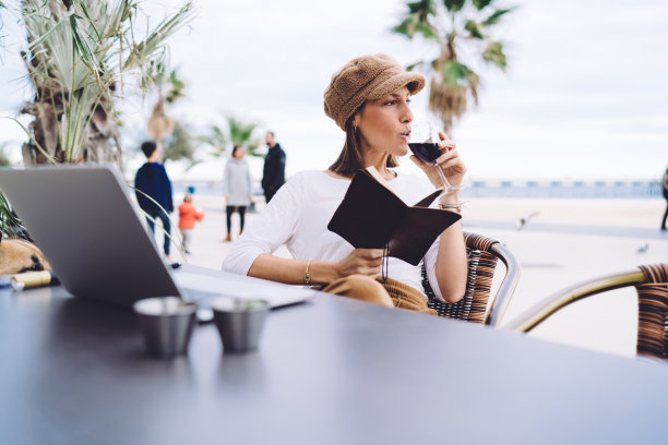 积极的女博主穿着时髦的衣服在咖啡馆露台上休息，喝着酒，漂亮的女人数字游牧民完成任务和在线项目喝红酒休息图片下载