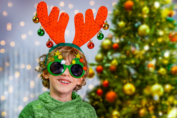 戴着滑稽驯鹿角的男孩听到了圣诞树的声音图片下载