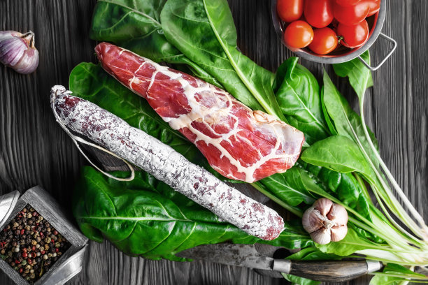 意大利腊肠和干肉夹在菠菜叶上的一层薄薄的脂肪网格里。切成青菜的意大利香肠图片下载