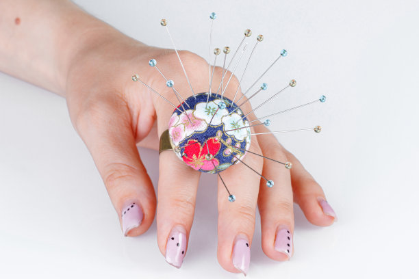 一枚戒指，在白色背景的手上有一个供针用的小枕头图片下载