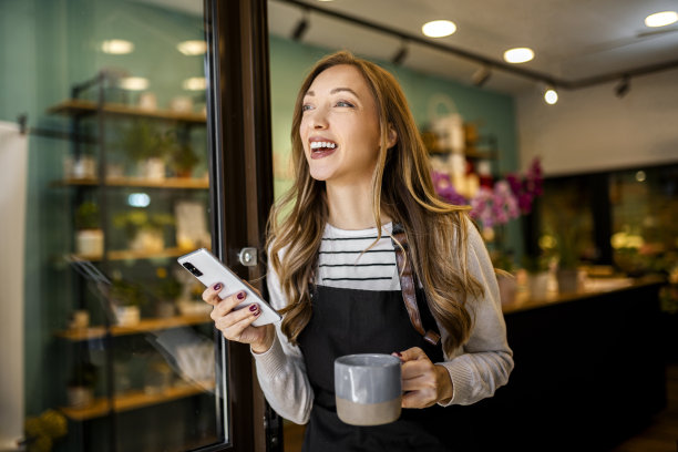 兴高采烈的年轻花商拿着智能手机在花店发短信图片下载