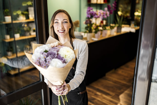 微笑的女花商与花束摆姿势在花店看着相机图片下载
