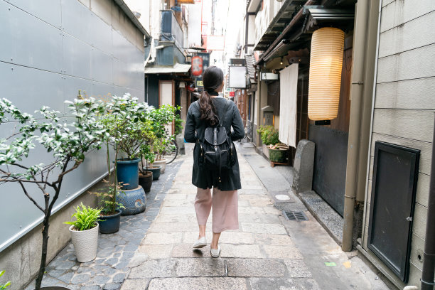 在日本大阪南巴eki，亚洲女性游客在传统的石头铺装和灯笼小巷中休闲散步的罕见全景。图片下载