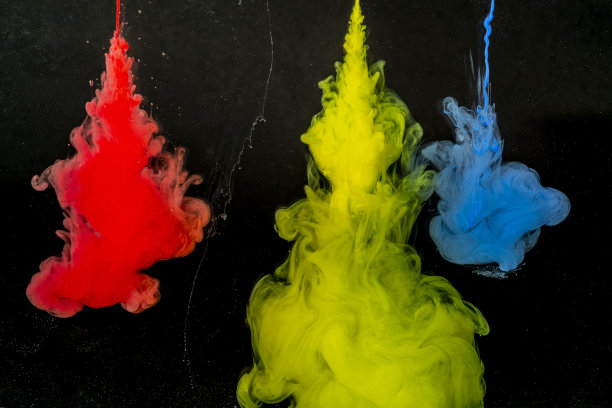 红色、黄色、蓝色和灰色的颜料从一根针流入黑色背景上的一碗水里图片下载