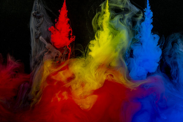 红色、黄色、蓝色和灰色的颜料从一根针流入黑色背景上的一碗水里图片下载