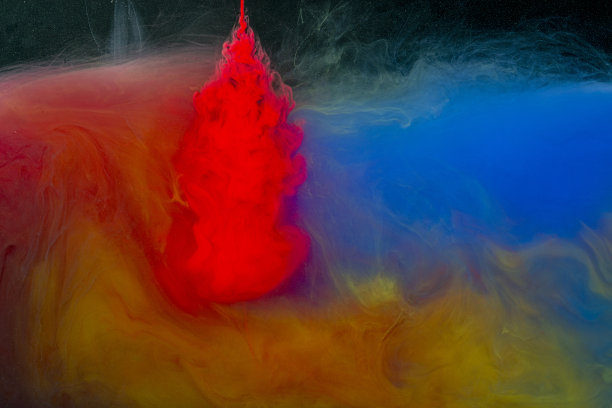 红色、黄色、蓝色和灰色的颜料从一根针流入黑色背景上的一碗水里图片下载