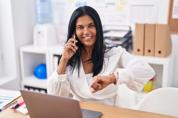 中年西班牙女性商务工作者在办公室用智能手机看手表说话图片下载