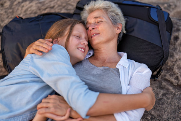 双肩包冒险徒步旅行者母女躺在山上拥抱微笑看着脸图片下载