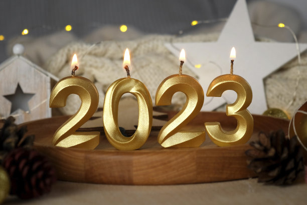 2023年新年黄金数字蜡烛在燃烧。背景中的模糊灯光。有礼物、装饰的新年贺卡。蝴蝶结和五彩纸屑。现代节日创意贺卡设计图片下载