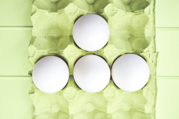 四个白鸡蛋装在绿色的纸盒里，放在绿色的桌子上图片下载