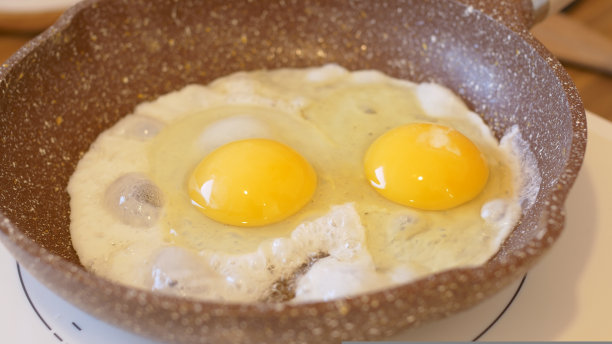特写煎锅与炒鸡蛋，另一个鸡蛋打破准备煎蛋。炒鸡蛋早餐，为一整天提供力量。日常准备炒鸡蛋早餐。图片下载