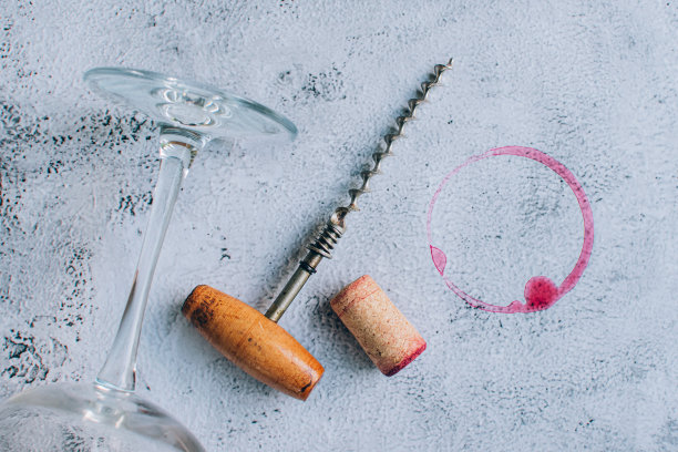 顶视图老式开瓶器，软木塞，葡萄酒杯和红色葡萄酒污渍在灰色背景图片下载