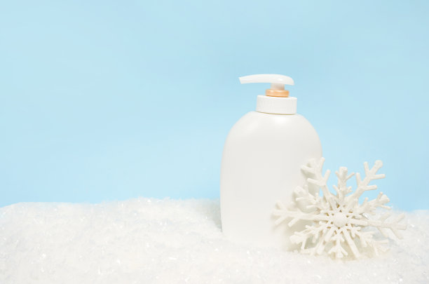 化妆品瓶洗剂或洗发水蓝色圣诞背景与雪和大雪花。冬季护肤图片下载