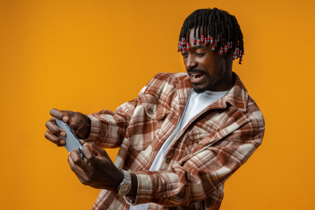 年轻的非洲男子穿着休闲装在黄色背景的手机上玩游戏。图片下载