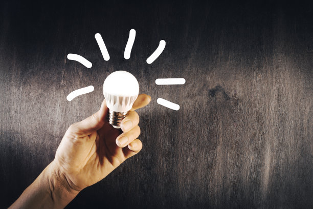 一个女人手里拿着一盏黑色木制背景的LED灯。节能技术。图片下载