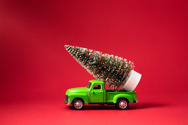 红色背景的绿色复古玩具车载着一棵圣诞树。圣诞节和新年庆祝概念。贺卡。复制空间，选择性聚焦图片下载