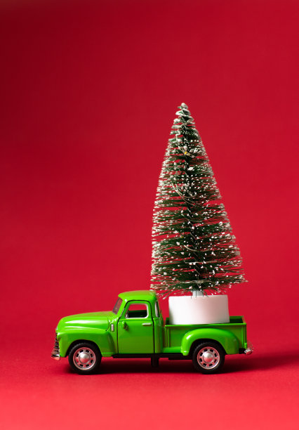 红色背景的绿色复古玩具车载着一棵圣诞树。圣诞节和新年庆祝概念。贺卡。复制空间，选择性聚焦图片下载