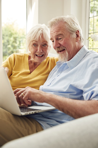 退休的老夫妇坐在家里的沙发上使用笔记本电脑图片下载