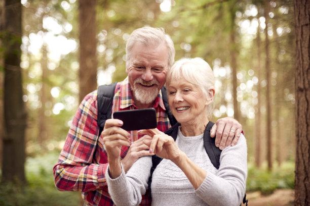 退休的老夫妇徒步林地乡村用手机拍照图片下载