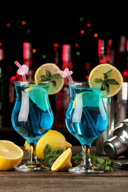 鸡尾酒蓝泻湖在鸡尾酒杯中，柠檬和薄荷放在酒吧的棕色木桌上。图片下载