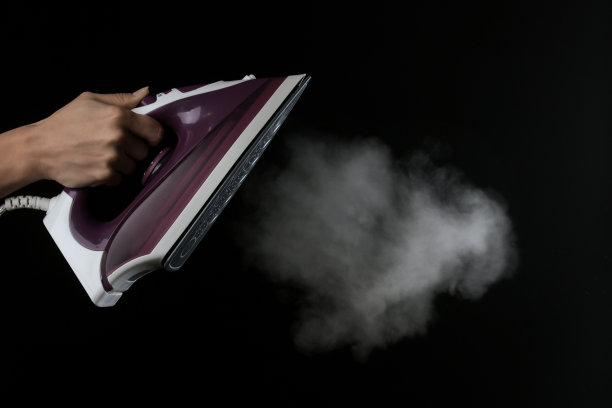 女孩在黑色的背景上从淡紫色的熨斗中喷出蒸汽。熨烫衣服。家用电器。图片下载