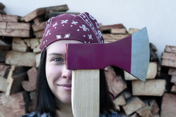 画像一个年轻的成年妇女微笑着站着，看着相机，拿着一把斧头在她的面前。在背景上收割柴火，准备迎接寒冷的冬天，以度过能源危机。图片下载