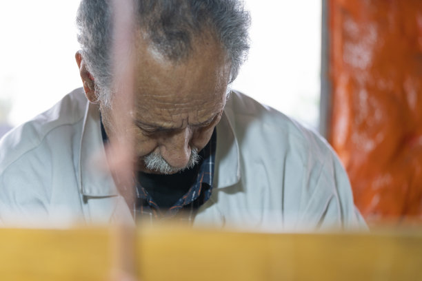 一个年纪较大的人，职业是工匠，在他的工厂里编织手工织布机。图片下载