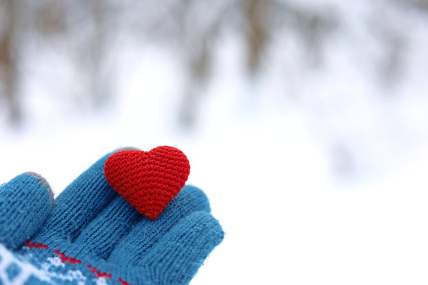 红色的心放在手掌上，戴着温暖的针织手套，在冬天的公园和雪地里图片下载