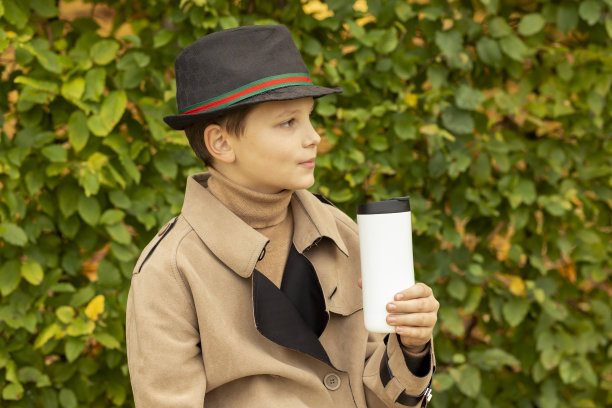 小男孩(十几岁)在公园户外用保温瓶(白色可重复使用的不锈钢咖啡杯杯)喝热茶，穿暖和的衣服米色外套、夹克。秋天的饮料。水平平面，复制空间图片下载