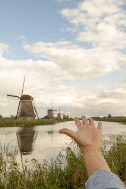 在荷兰肯德迪克，一个年轻的男性正在开心地张开双臂的视角拍摄。  在一个日落的秋天下午，从个人的角度拍摄，在背上，风车。图片下载