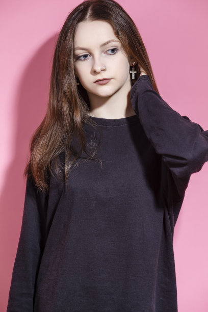 严肃的金发少女肖像在卫衣专心地看着相机，而摆姿势与举起的手在工作室孤立的粉红色背景图片下载