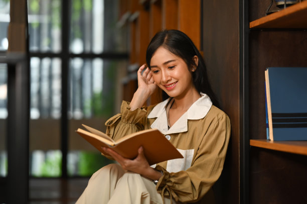 迷人的年轻女子站在书架旁边看书。人、知识、教育观念。图片下载