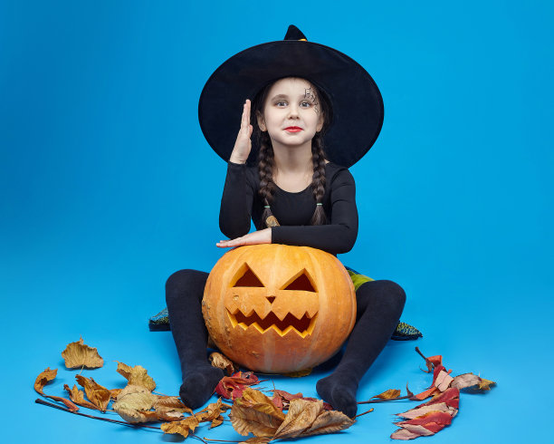 一个穿着女巫服装的迷人小女孩的肖像，杰克的灯站在周围。万圣节的概念图片下载