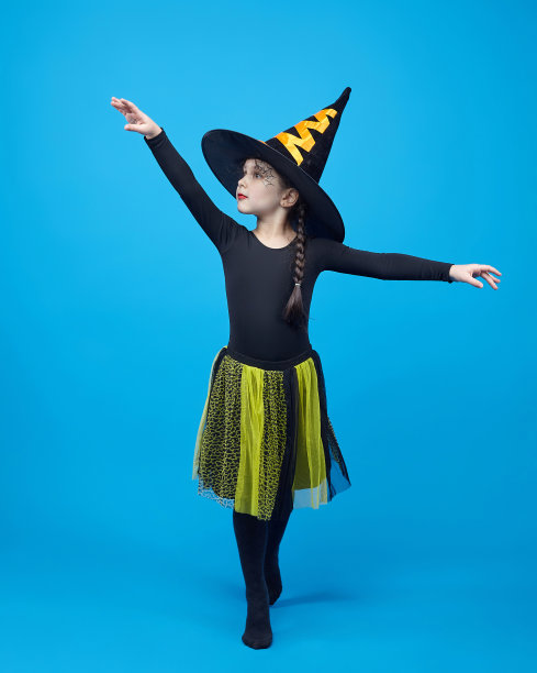 迷人的小女孩穿着女巫服装在蓝色背景的工作室跳舞图片下载