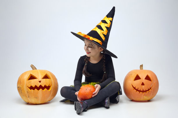 一个穿着女巫服装的迷人小女孩的肖像，杰克的灯站在周围。万圣节的概念图片下载