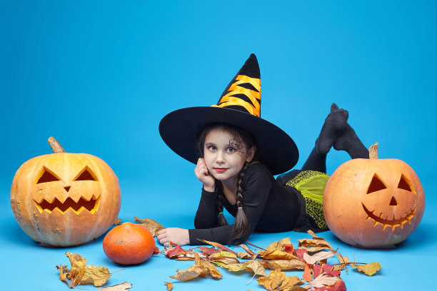 一个穿着女巫服装的迷人小女孩的肖像，杰克的灯站在周围。万圣节的概念图片下载
