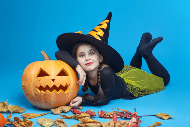 一个穿着女巫服装的迷人小女孩的肖像，杰克的灯站在周围。万圣节的概念图片下载
