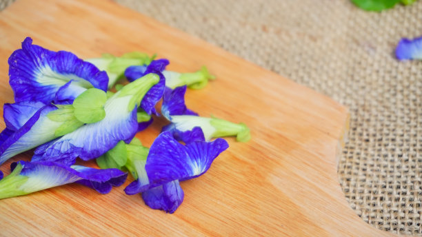 木板上一堆蝴蝶豌豆花(蝶豆)，背景是粗麻布，特朗花为凉茶原料-平铺概念图片下载