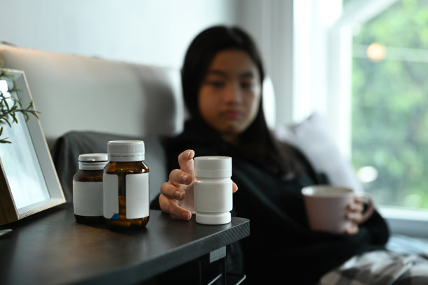 生病的年轻女子在卧室用一杯水吃药。保健和医疗概念。图片下载