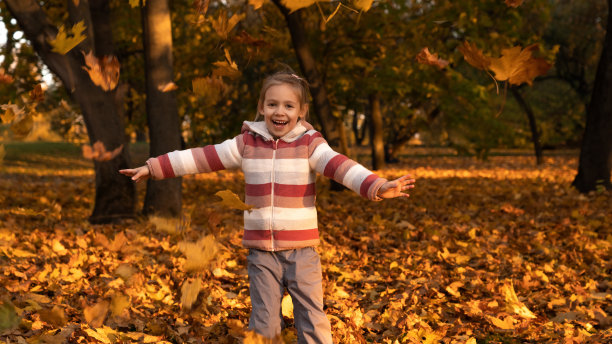 女孩在秋天的公园里玩树叶。孩子笑着把树叶扔到户外图片下载
