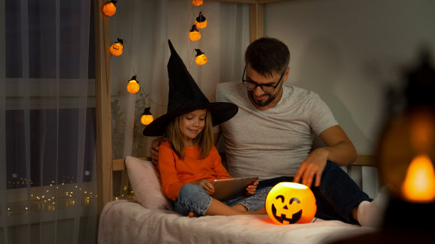 父亲和女儿用南瓜灯在平板电脑上看恐怖电影。万圣节图片下载