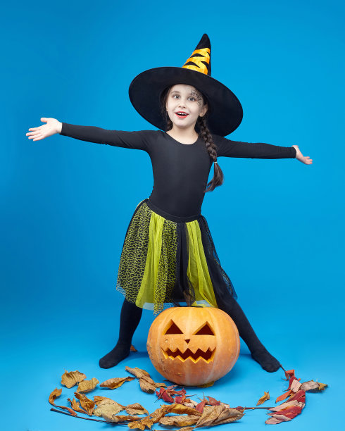 一个穿着女巫服装的迷人小女孩的肖像，杰克的灯站在周围。春节的概念图片下载