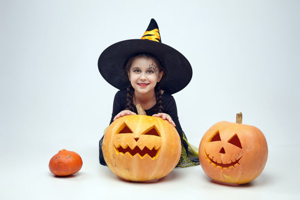 一个穿着女巫服装的迷人小女孩的肖像，杰克的灯站在周围。春节的概念图片下载