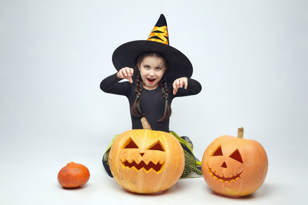 一个穿着女巫服装的迷人小女孩的肖像，杰克的灯站在周围。春节的概念图片下载