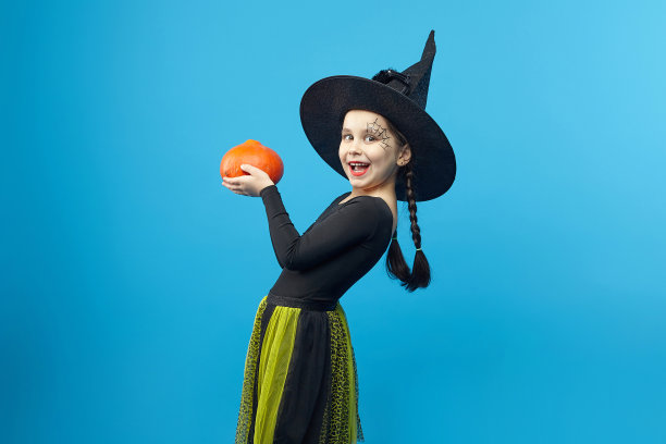 一个穿着女巫服装的迷人小女孩的肖像，杰克的灯站在周围。春节的概念图片下载