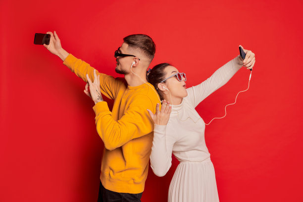 幸福的年轻夫妇的肖像，男人和女人，背靠背站着，在红色背景隔离的电话上进行视频通话图片下载