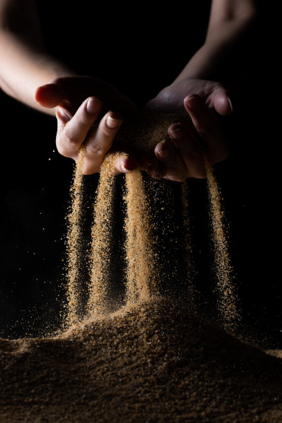 手释放掉沙。细沙在黑色背景下从手指间流淌。暑假海滩度假和时光流逝的概念。隔离式高速快门图片下载